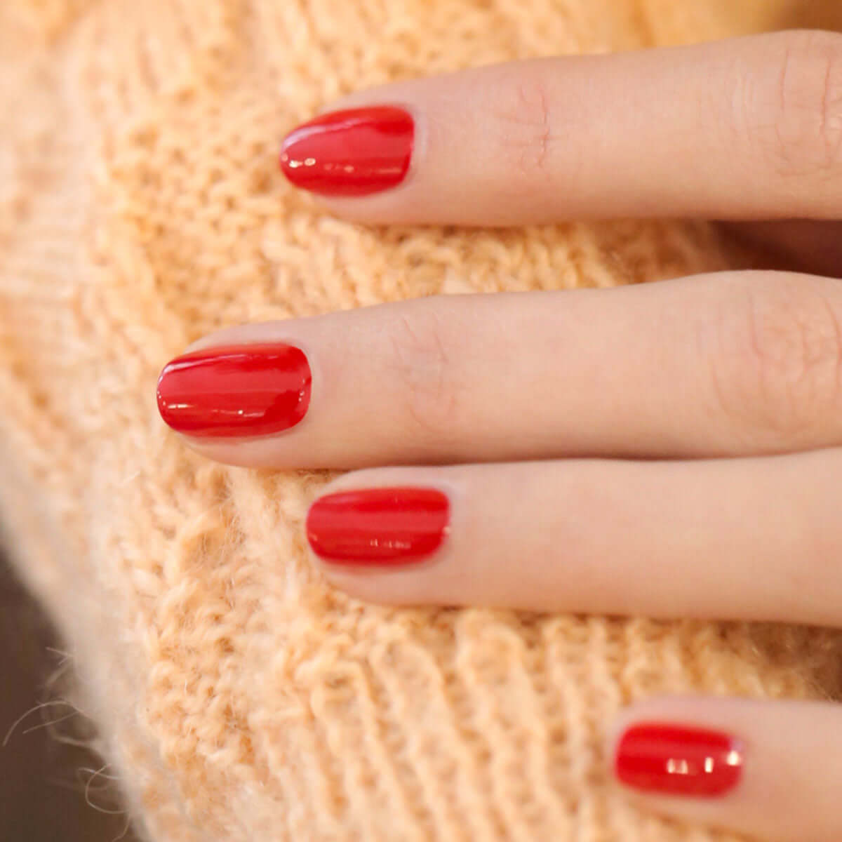 Bright Poppy Red nail polish on fingers, showcasing a vibrant orangey-red shade - Living Beauty.